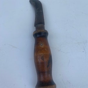 May include: A vintage, curved-blade knife with a wooden handle. The blade is made of metal and has a dark brown patina. The handle is made of wood and has a dark brown finish. The knife is in good condition and has a sharp blade.