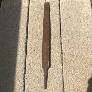May include: A rusty metal file with a pointed end. The file is about 12 inches long and has a rough surface.
