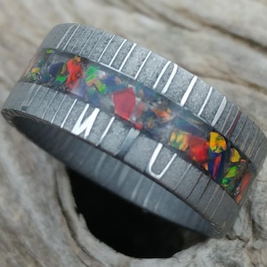 Può includere: Un anello d'argento con una fascia di intarsi di opale colorati. L'anello ha una finitura testurizzata e una sottile scanalatura che corre attorno alla fascia.