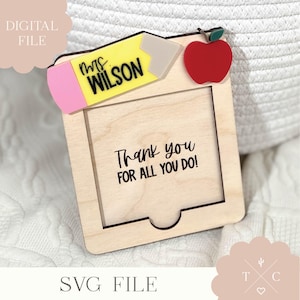 May include: A wooden frame with a cutout for a photo. The frame is decorated with a red apple, a yellow pencil with a pink eraser, and the text "Mrs. Wilson". The frame also has the text "Thank you for all you do!"