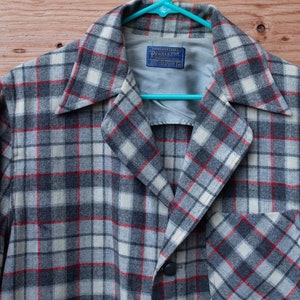 May include: A gray, red, and white plaid flannel shirt with a button closure and a pocket on the left side. The shirt has a label that reads "Pendleton" in blue.