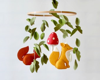 May include: A wooden mobile with felt woodland animals, including a fox, squirrel, and mushroom. The mobile features green felt leaves hanging from the wooden ring.