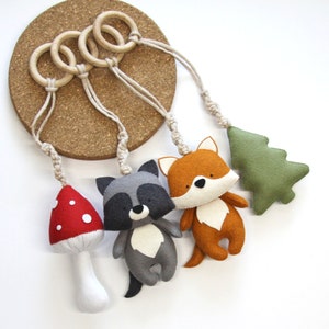 May include: A felt woodland animal mobile with a fox, raccoon, mushroom, and a green tree. The mobile is hung from wooden rings.