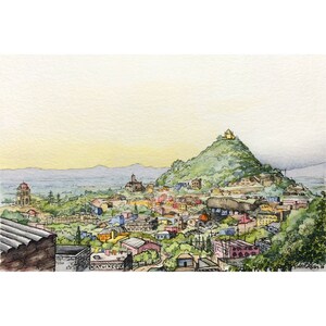 Pu&ograve; includere: Un dipinto ad acquerello che rappresenta una citt&agrave; con una collina sullo sfondo. La collina &egrave; ricoperta di alberi verdi e ha un piccolo edificio in cima. La citt&agrave; &egrave; composta da molti piccoli edifici, alcuni dei quali sono dipinti con colori vivaci. Il cielo &egrave; azzurro chiaro e ci sono nuvole in lontananza.