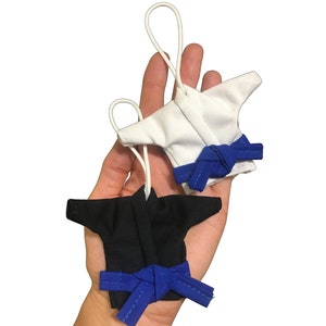 Puede incluir: Dos uniformes de karate en miniatura con cinturones azules. Un uniforme es blanco y el otro es negro.