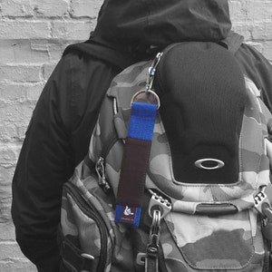 May include: A black and camouflage backpack with a blue and brown key chain attached. The keychain has a small white symbol on it.