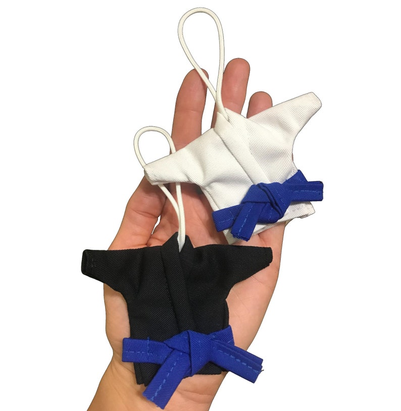 Puede incluir: Dos uniformes de karate en miniatura con cinturones azules. Un uniforme es blanco y el otro es negro.