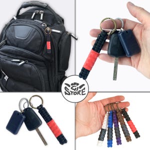 May include: A collection of paracord keychains featuring a braided black cord with a solid red center section attached to a metal ring. The keychains are shown attached to a black backpack, holding car keys, and in a multi-colored set of five.