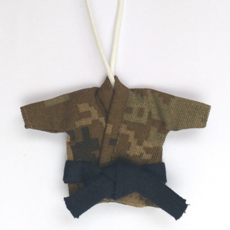 Puede incluir: Uniforme de karate en miniatura con estampado de camuflaje y cintur&oacute;n negro, colgado de una cuerda blanca.