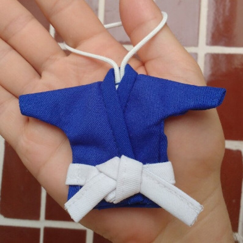 Puede incluir: Uniforme de karate azul en miniatura con cintur&oacute;n blanco. El uniforme est&aacute; atado a la cintura y tiene un dise&ntilde;o tradicional de karate.