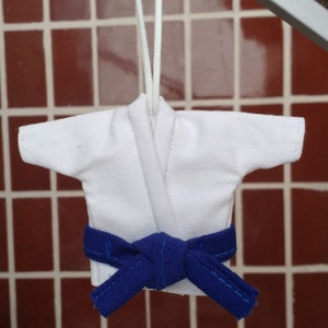 Puede incluir: Uniforme de karate blanco con un cintur&oacute;n azul atado a la cintura. El uniforme est&aacute; colgado de una cuerda.