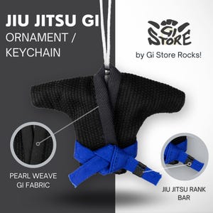 Op de afbeelding: Een zwarte jiu-jitsu gi-versiering of sleutelhanger met een blauwe riem. De gi is gemaakt van parelweefsel en heeft een jiu-jitsu rangbalk. De versiering is gemaakt door Gi Store Rocks.