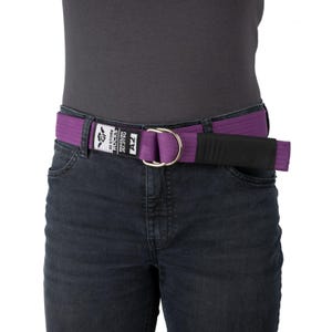May include: A purple belt with a D-ring buckle is worn over dark denim jeans. The belt has a black velcro closure and a white tag with the text "GI STORE ROCKS BRAZILIAN JIU JITSU" and the letters "A2".