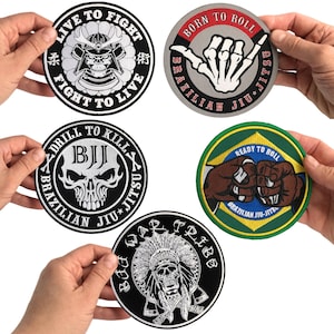 May include: Five circular embroidered patches featuring martial arts themes. Designs include a samurai skull with 'Live to Fight, Fight to Live', a skeleton hand with 'Born to Roll', a skull with 'Drill to Kill', a fist bump over a flag, and a skull in a headdress.