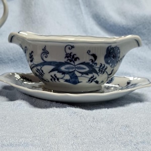 May include: A white porcelain gravy boat with a blue and white floral pattern. The boat is sitting on a matching saucer.