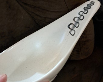 May include: White ceramic serving dish with a long, pointed shape and a black and white design of a series of connected loops on the top edge.