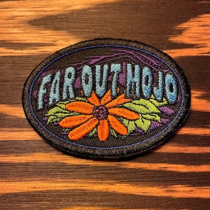 May include: A black and blue embroidered patch with the text "Far Out Mojo" in a blue and white font. A large orange flower with a purple center is in the middle of the patch.