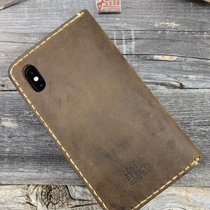 May include: A brown leather phone case with a stitched border and the words "LONE DEER Leather Co." stamped on the lower right. The case is on a wooden surface with leatherworking tools.