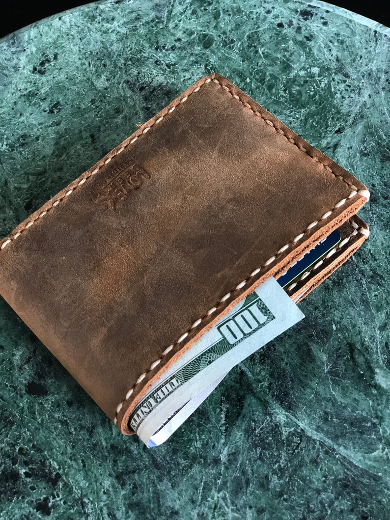 May include: A brown leather wallet with white stitching and a bill sticking out. The wallet has the text "Leather" embossed on the front.