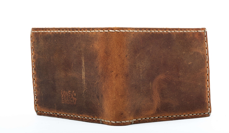May include: A brown leather wallet with white stitching and the text "Lone Deer" embossed on the front.