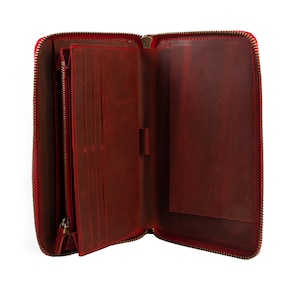 May include: A red leather zippered wallet with multiple card slots and a large pocket. The wallet is open and empty.