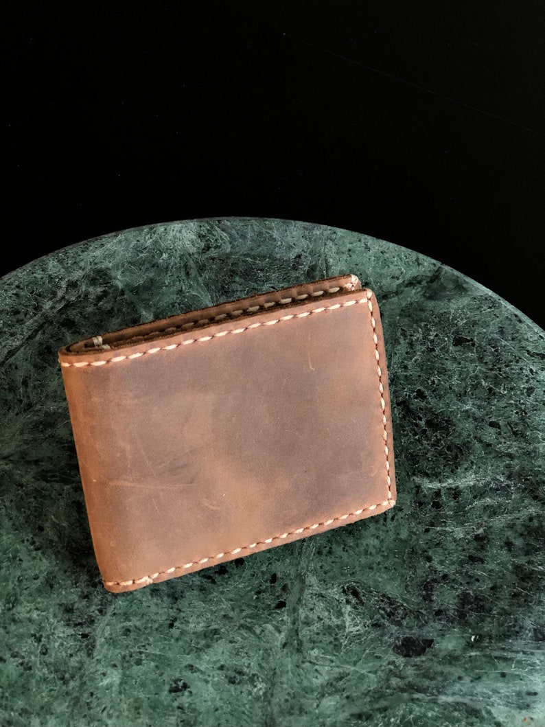 May include: A brown leather wallet with white stitching on a green marble surface.
