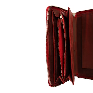 May include: A red leather zippered wallet with a gold zipper. The wallet is open and the inside is visible.
