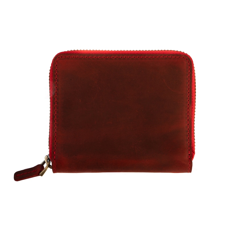 May include: A small, red leather zippered wallet. The wallet is made of a soft, distressed leather and has a zipper closure.