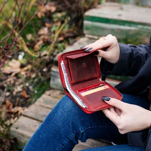 May include: A red leather zippered wallet with a zipper pull, open to reveal cash and credit cards.