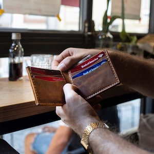 May include: A brown leather wallet with a flap closure, open to reveal three credit cards, two of which are from Bank of America.