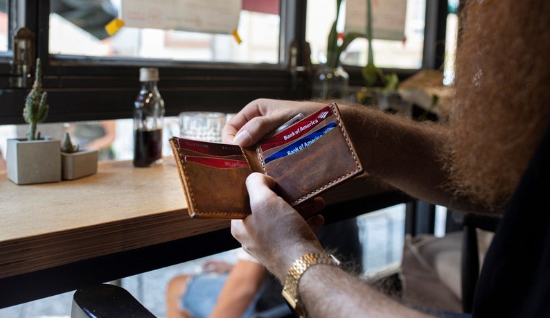 May include: A brown leather wallet with a flap closure, open to reveal three credit cards, two of which are from Bank of America.