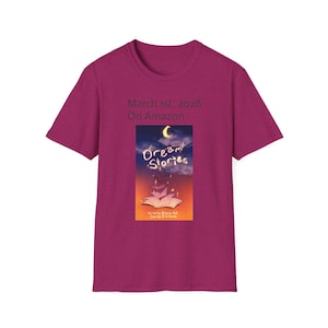 May include: A magenta t-shirt featuring the text "March 1st, 2026 On Amazon." The shirt displays a book cover design with the title "Dream Stories" under a crescent moon and stars. The book cover has a warm color palette.