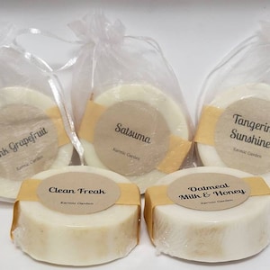 May include: Five round bars of soap in individual clear organza bags. The soap bars are white with a yellow stripe around the edge. Each bar has a round label with a different scent name: Pink Grapefruit, Satsuma, Tangerine Sunshine, Oatmeal Milk & Honey, and Clean Freak.