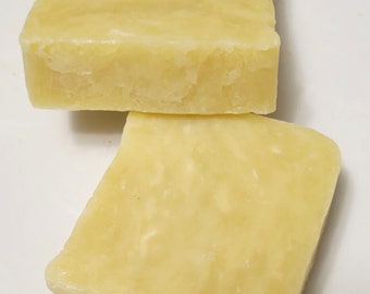 May include: Two rectangular bars of solid, pale yellow soap. Each bar features a smooth, slightly textured surface with subtle variations in color tone throughout the material. The bars are stacked slightly offset from one another, showing their thickness.
