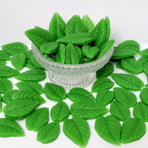 May include: A bowl filled with green wax leaves, surrounded by more green wax leaves on a white surface.