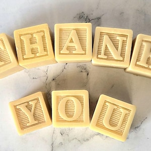 May include: Cream-colored wooden blocks spelling out "THANK YOU". Each block features a letter in a bold, serif font. The blocks are arranged in a semi-circular pattern against a light background, creating a simple, yet elegant design.