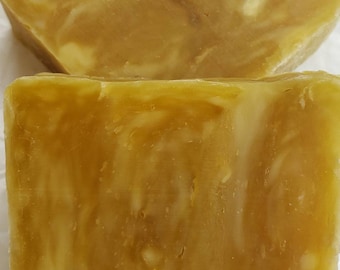 May include: Two rectangular bars of soap with a marbled appearance in shades of golden yellow, amber, and cream. The surface of the soap has a smooth, slightly translucent texture with visible swirls of lighter and darker tones throughout the bars.