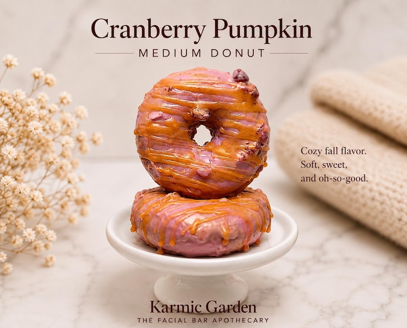 May include: Two stacked cranberry pumpkin medium donut-shaped bars with pink glaze and caramel-colored drizzle on a white pedestal. Text reads: Cranberry Pumpkin, MEDIUM DONUT, Cozy fall flavor. Soft, sweet, and oh-so-good. Karmic Garden THE FACIAL BAR APOTHECARY.