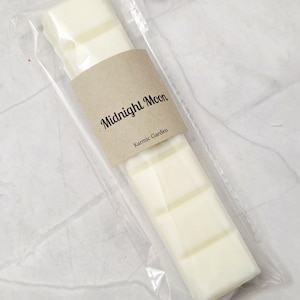 May include: A white wax melt bar with the text "Midnight Moon" and "Karmic Garden" on a brown label. The bar is packaged in a clear plastic bag.