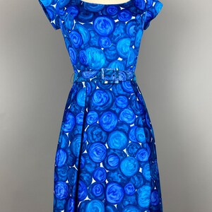 May include: A blue and white vintage dress with a circle pattern. The dress has a scoop neckline, short sleeves, and a fitted bodice. It is belted at the waist and has a full skirt.