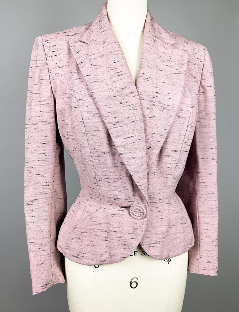 Puede incluir: Una chaqueta rosa con un cierre de bot&oacute;n &uacute;nico y una silueta ligeramente ajustada. La chaqueta tiene un patr&oacute;n moteado en toda su superficie.