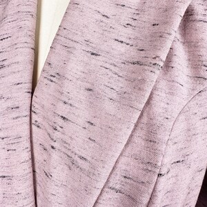 Puede incluir: Primer plano de una chaqueta rosa con un sutil patr&oacute;n de motas negras. La tela es texturizada y tiene un ligero brillo.