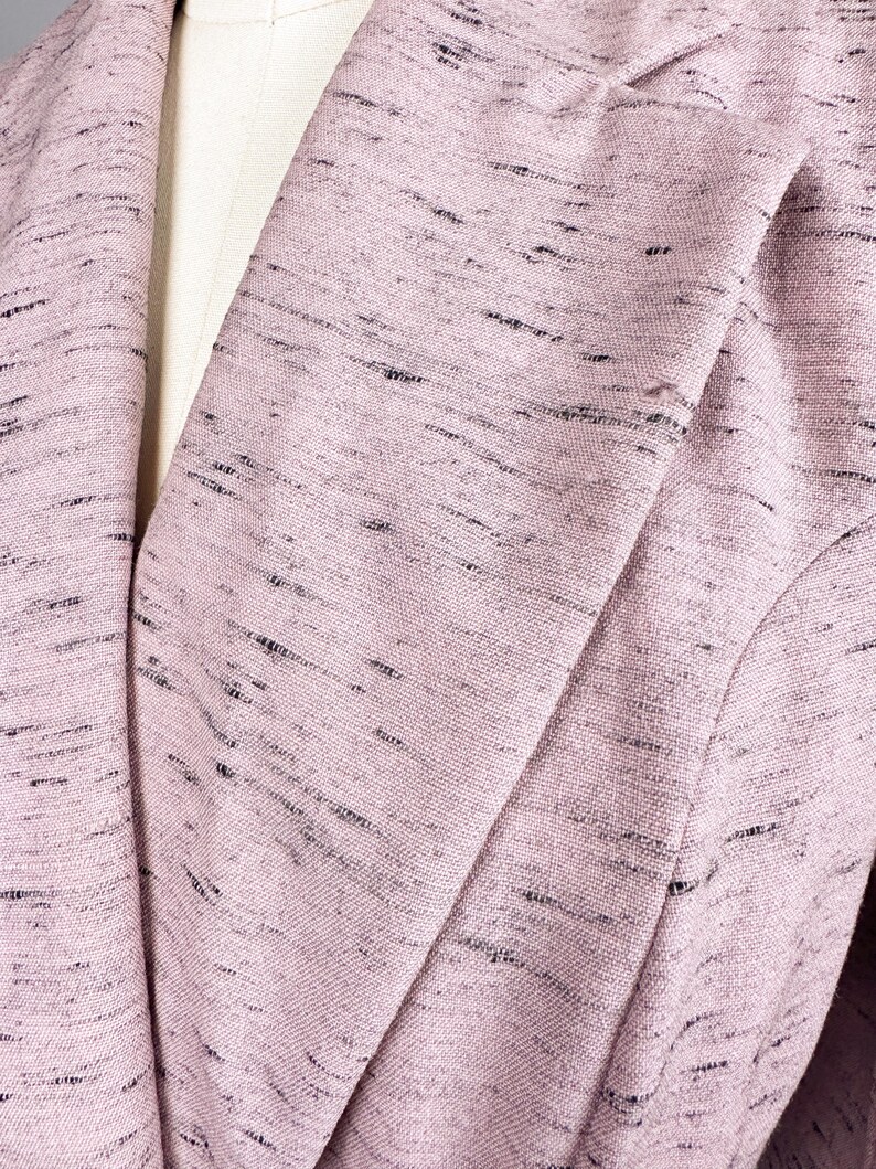Puede incluir: Primer plano de una chaqueta rosa con un sutil patr&oacute;n de motas negras. La tela es texturizada y tiene un ligero brillo.