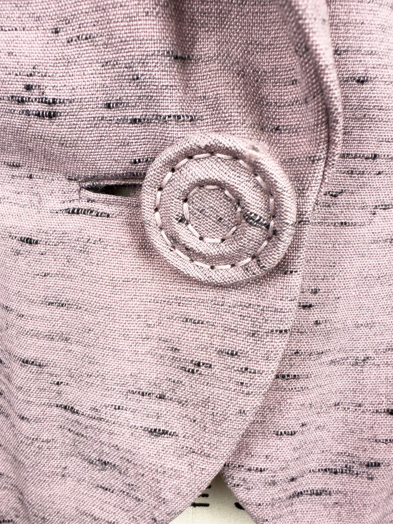 Puede incluir: Primer plano de una tela rosa con un patr&oacute;n moteado en blanco y negro. Un bot&oacute;n grande y redondo est&aacute; cosido en la tela.