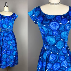 May include: A blue and white vintage dress with a circle pattern. The dress has a scoop neck, short sleeves, and a fitted bodice. It has a full skirt and a belt at the waist.