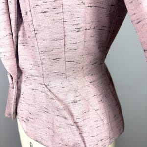 Puede incluir: Una chaqueta rosa con tejido texturizado y cintura ajustada. La chaqueta tiene un dobladillo ligeramente acampanado y manga tres cuartos.