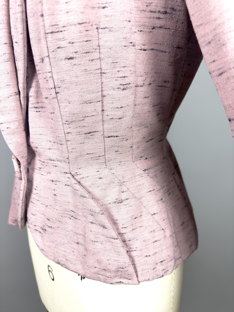 Puede incluir: Una chaqueta rosa con tejido texturizado y cintura ajustada. La chaqueta tiene un dobladillo ligeramente acampanado y manga tres cuartos.