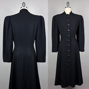 May include: A black long-sleeved dress with a fitted bodice and a flared skirt. The dress has a high neckline and a row of buttons down the front.
