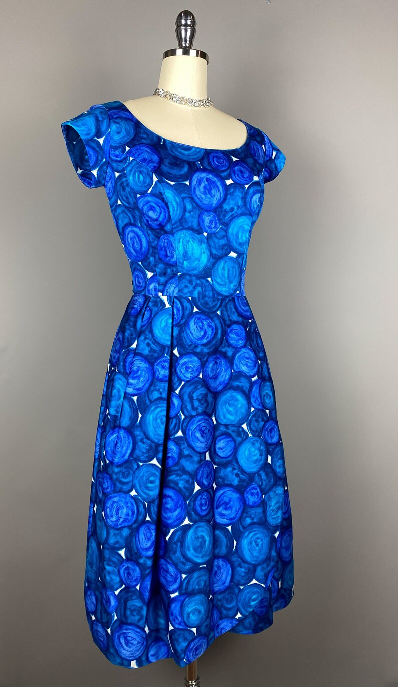 May include: A blue and white vintage dress with a circle pattern. The dress has a scoop neck and short sleeves.