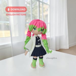 May include: A crochet doll featuring long pink and green braided hair, wearing a white haori over a dark blue uniform with a white belt, and green leg warmers. The image includes text that reads DOWNLOAD ENGLISH PATTERN and @huongkhvn.